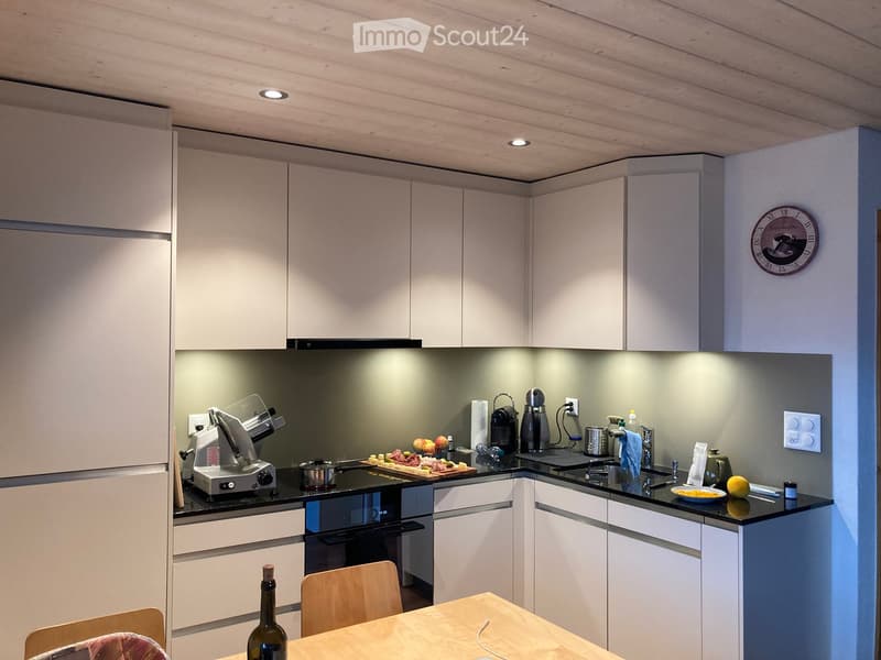 Modern kitchen with white cabinets, black countertops, stainless steel appliances, and a small dining area with a wooden table and chairs.