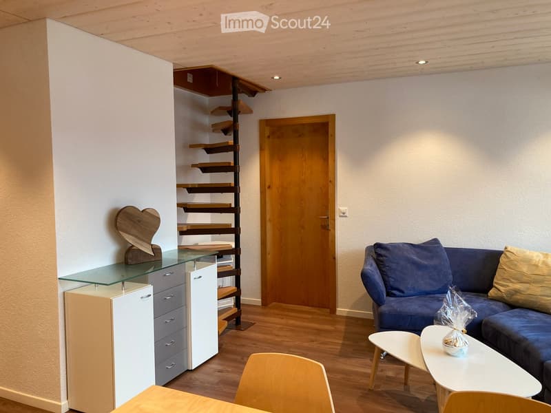 Modern living room with a blue sofa, white coffee table, wooden chairs, glass cabinet, and wooden shelving unit.