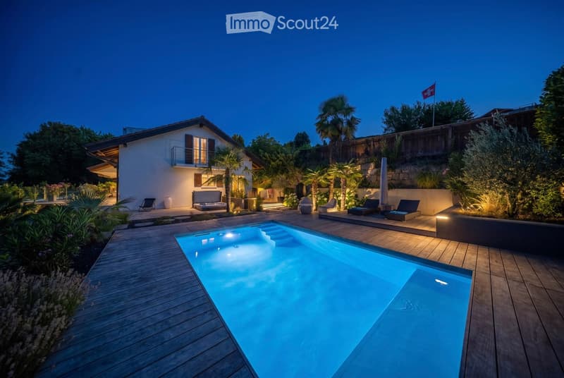Evening view of a modern house with a swimming pool, surrounded by palm trees and lounge chairs.