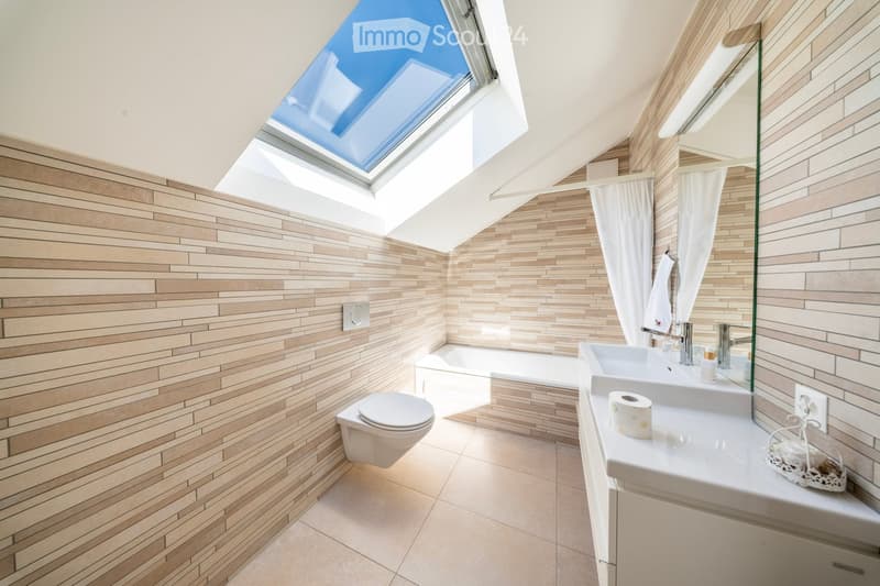 Modern bathroom with light wood tile walls and floor, a skylight window, a toilet, a bathtub, a double sink with a mirror, and a curtain.