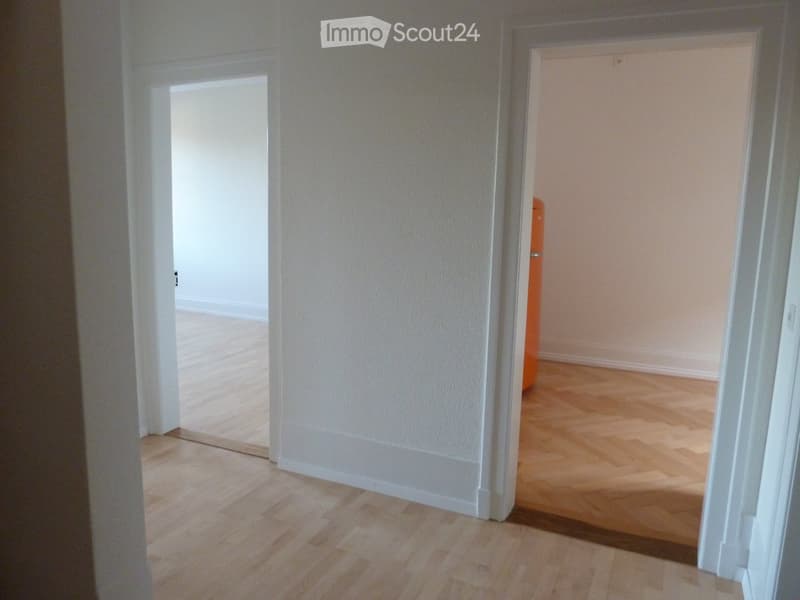 Empty hallway with light wooden flooring and white walls, featuring two open doorways leading to adjacent rooms.