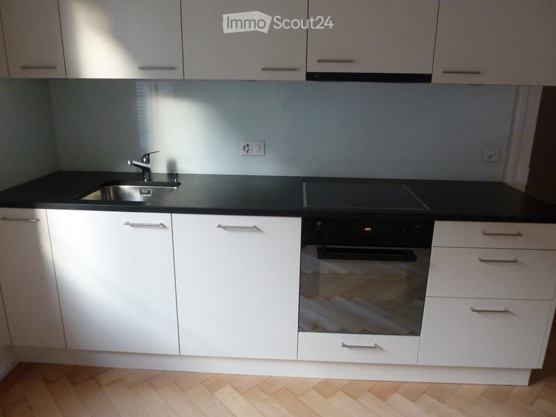 Modern kitchen with white cabinets, black countertops, stainless steel sink, and built-in oven.