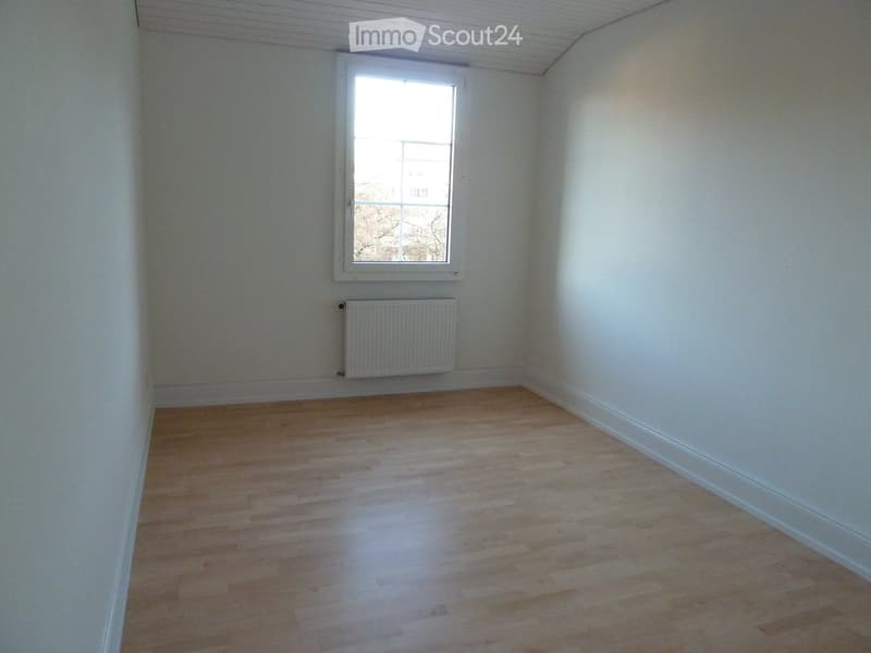 Empty room with light wooden flooring, white walls, a single window, and a radiator below it.