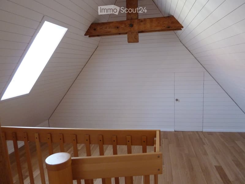 Empty attic space with wooden floor, white paneled walls, skylight window, and exposed wooden beam ceiling structure.