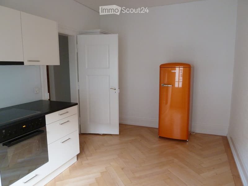 Modern kitchen with light wooden flooring, white cabinets, a black countertop, and a vintage-style orange refrigerator.