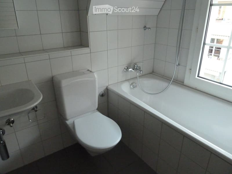 Bathroom with white tiled walls and floor, featuring a toilet, bathtub, and sink.