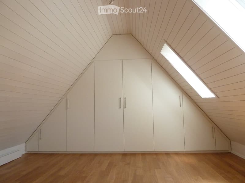 An attic room with wooden floors, white built-in wardrobes, and a skylight window providing natural light.