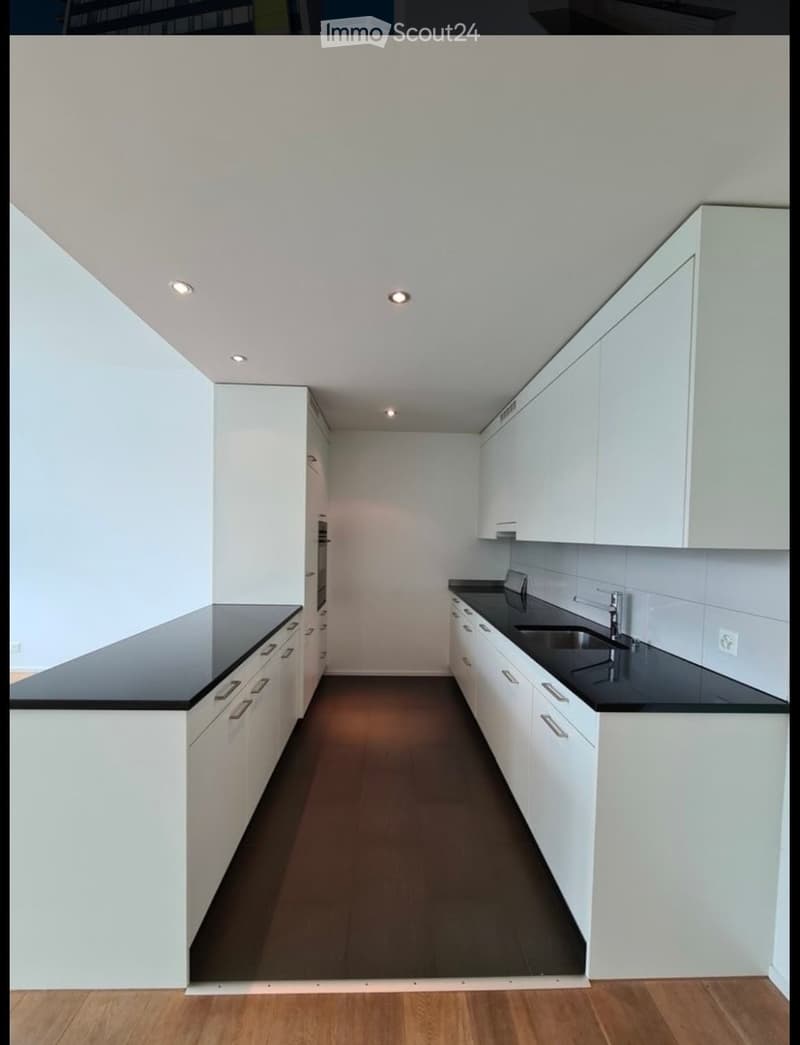 Modern kitchen with white cabinets, black countertops, and a dark floor. Features a sink with a modern faucet and recessed lighting.