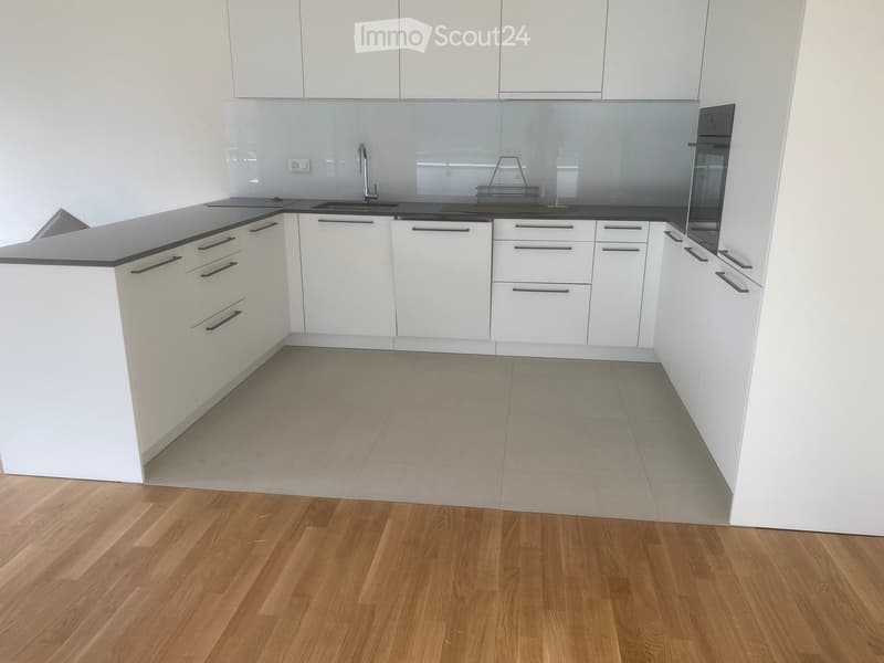 Modern kitchen with white cabinets, black countertops, and a wooden floor. Features a sink, faucet, and oven.