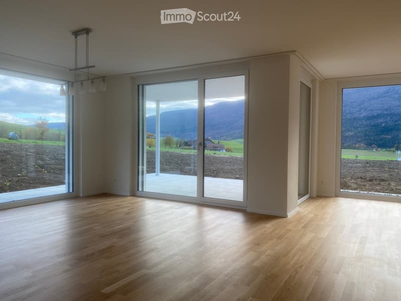 Empty room with wooden flooring, large windows, and sliding glass doors leading to a patio with a scenic mountain view.