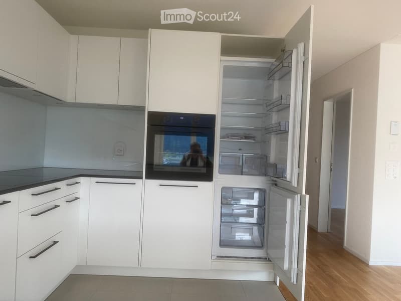 Modern kitchen with white cabinets, black countertops, and stainless steel appliances including an open refrigerator and oven.