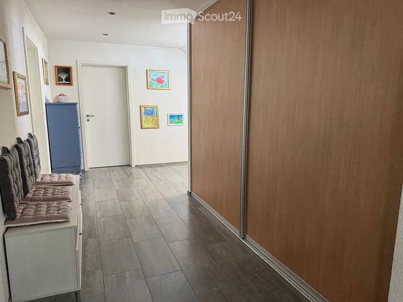 Hallway with tiled floor, wooden wall paneling, framed artwork, and a small bench with cushions.
