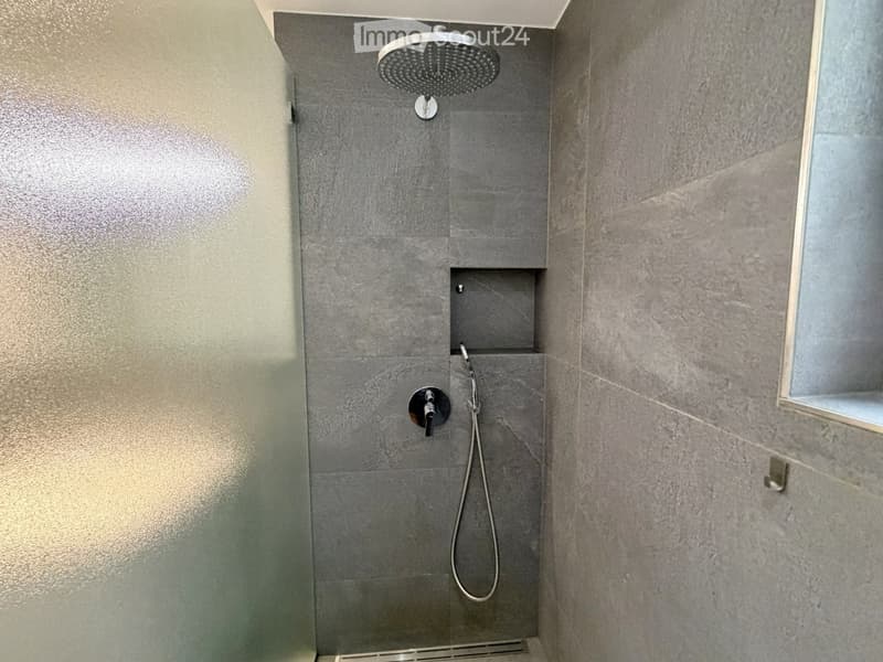 Modern shower area with grey tiled walls, a built-in shelf, and a handheld showerhead with a hose.