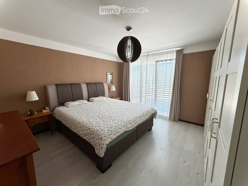 Modern bedroom with a large bed, nightstands, lamps, and a large window with curtains.