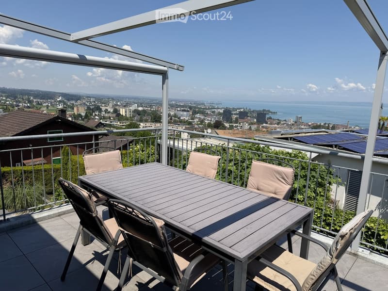 Balcony with a table and chairs, overlooking a scenic city and lake view.