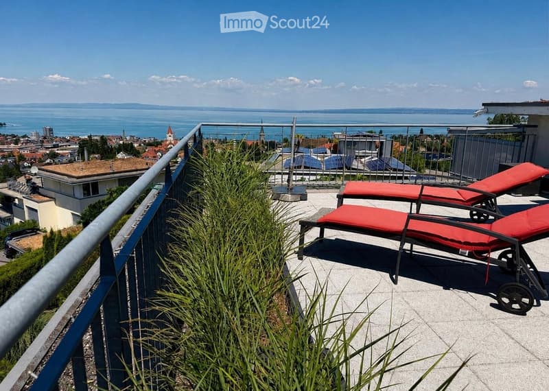 Balcony with sun loungers, overlooking a scenic lake and cityscape.