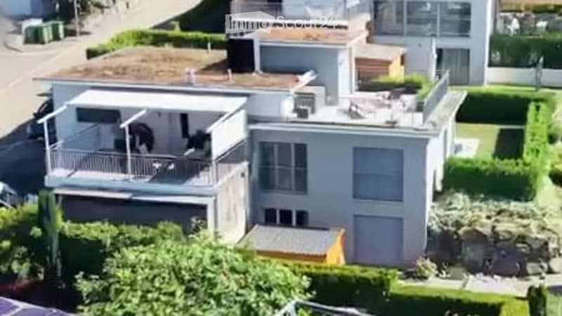 Modern two-story house with a flat roof, large windows, and a balcony on the upper level.