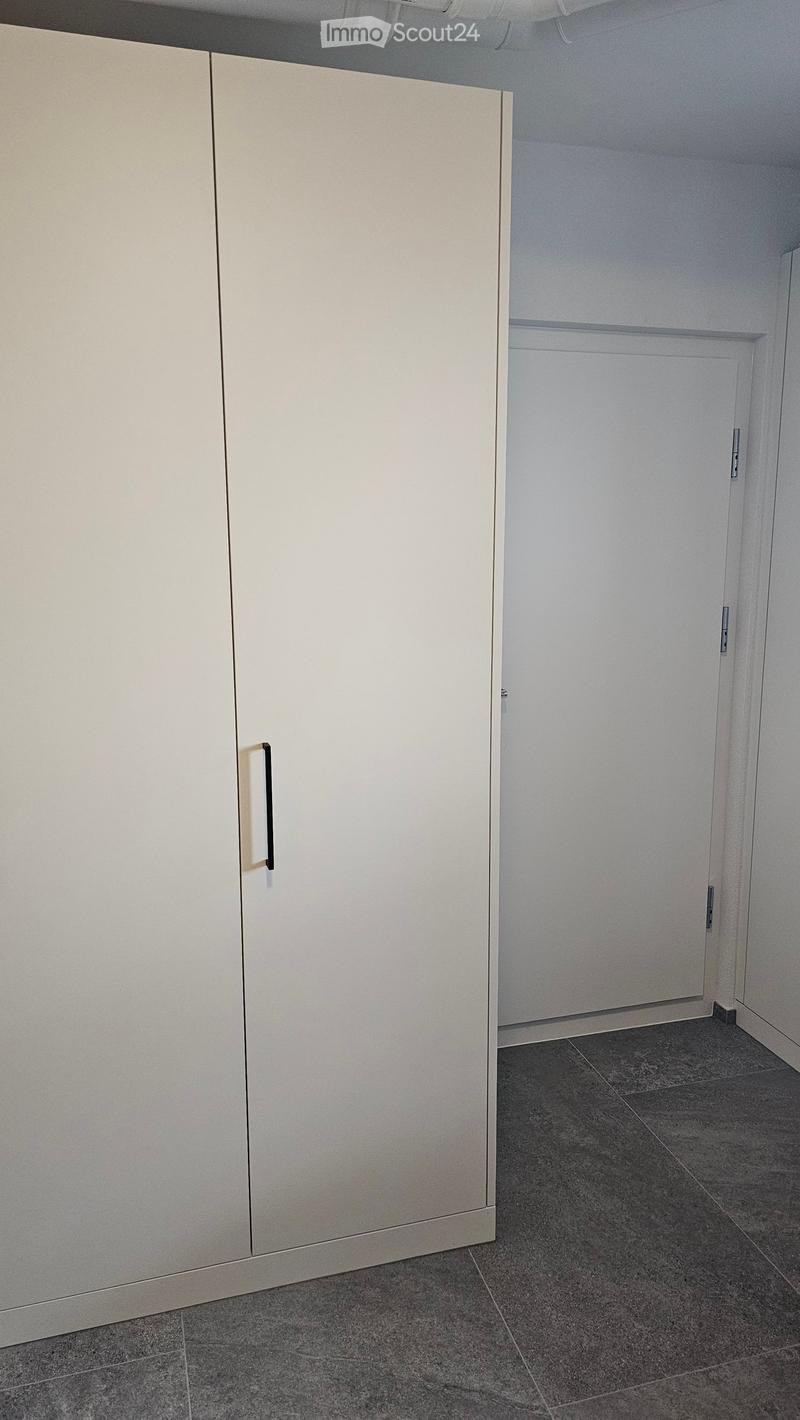 Empty room with grey tiled floor, white walls, and a large white cabinet with a handle on the left side.