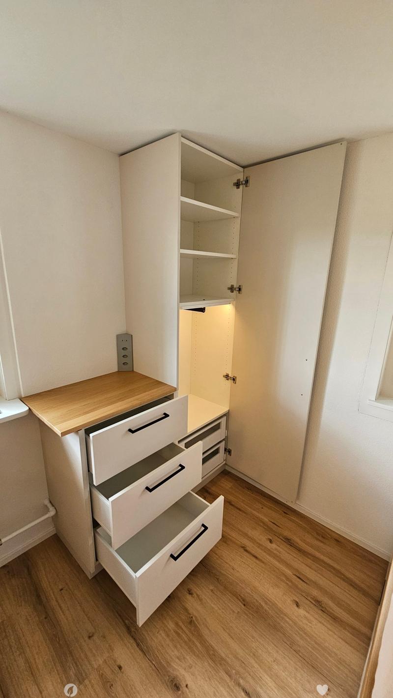 Empty room with light wooden flooring, white walls, and built-in white cabinetry with open shelves and drawers.