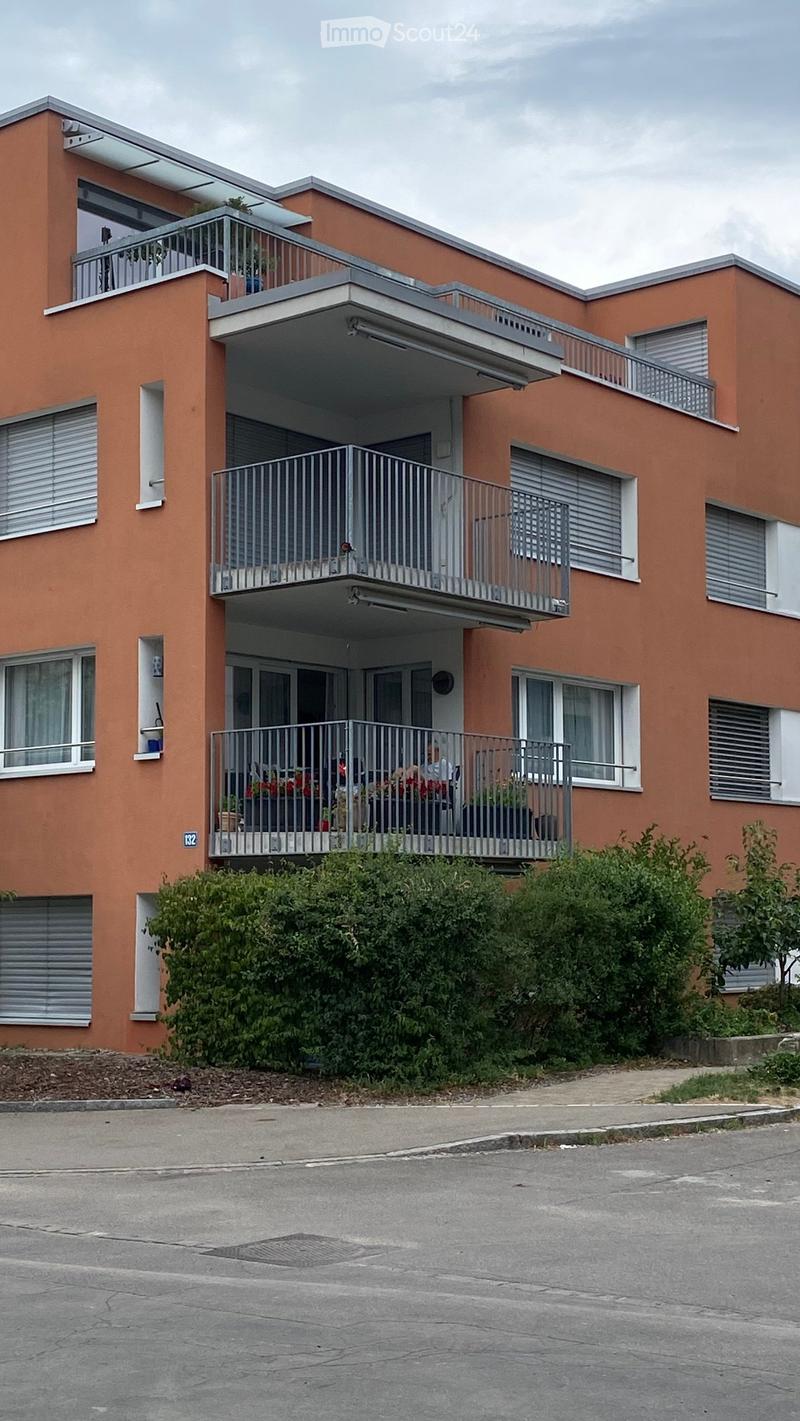 Modern three-story apartment building with orange facade, multiple balconies, and greenery in front.