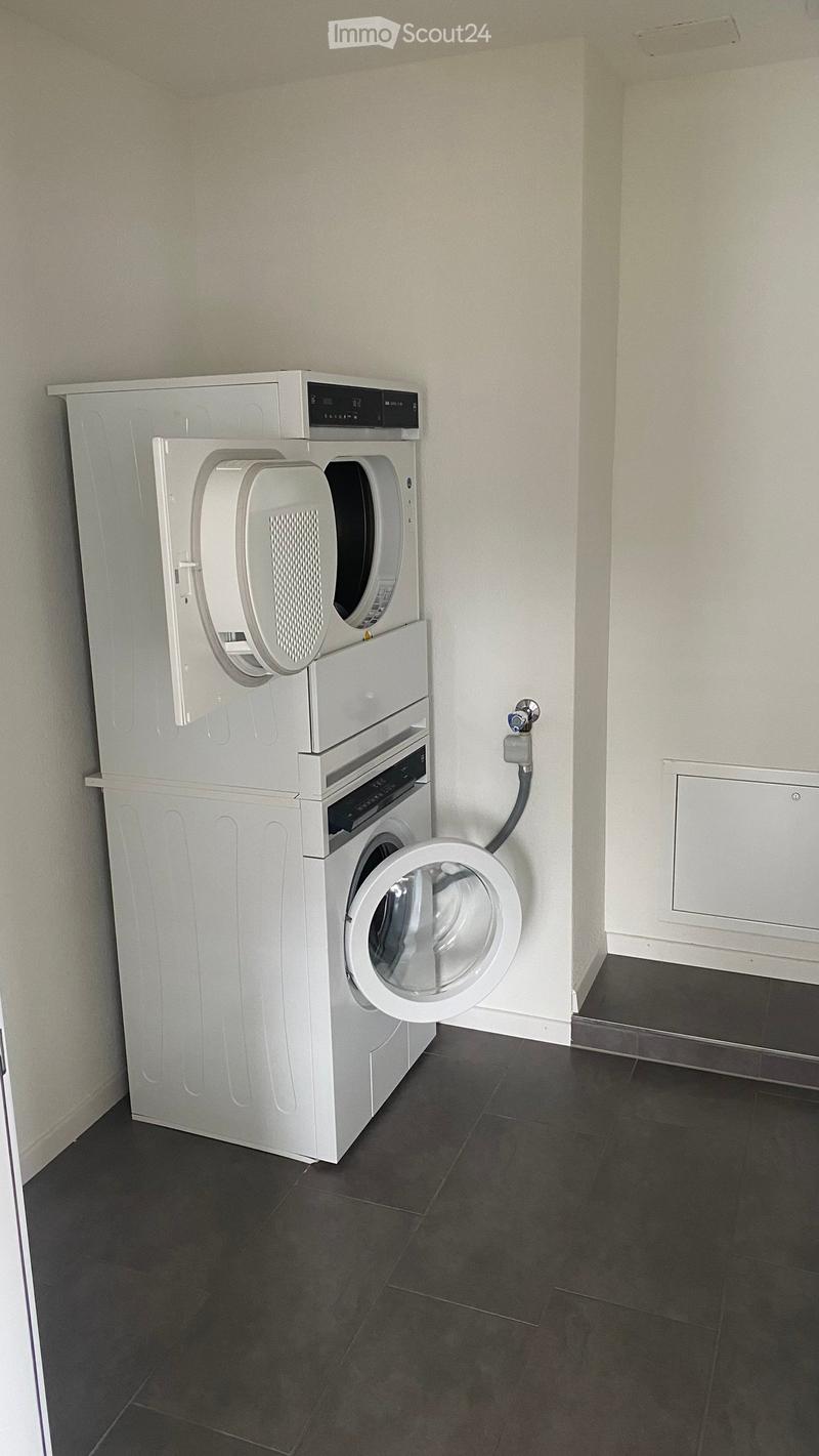 A small room with a stacked washing machine and dryer unit against a wall, featuring a dark tiled floor and light-colored walls.