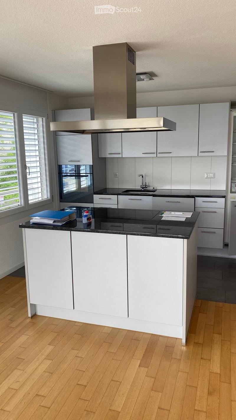 Modern kitchen with white cabinets, stainless steel appliances, black countertop, and wooden flooring.