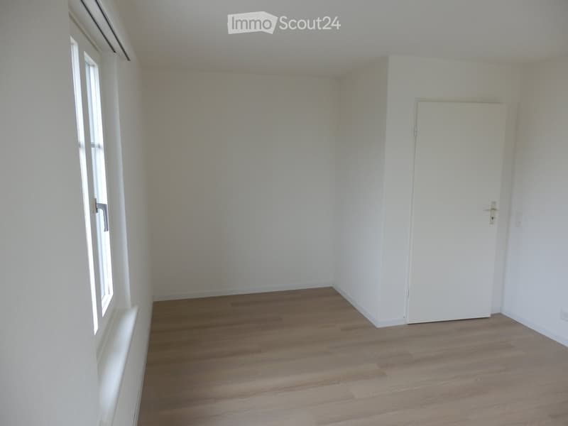 Empty room with white walls, wooden flooring, and a single door. No furniture or equipment present.
