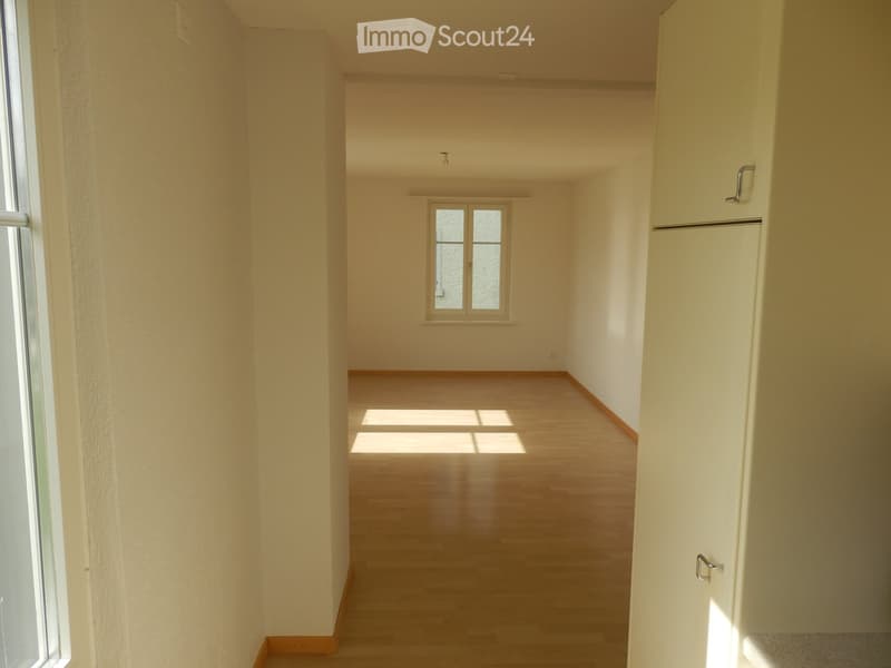 Empty room with wooden flooring and white walls, featuring a window at the far end and a door on the right side.