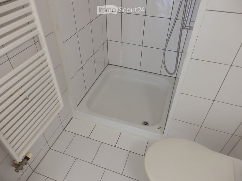 Bathroom with white tiled walls and floor, featuring a bathtub, toilet, and a white radiator on the left side.