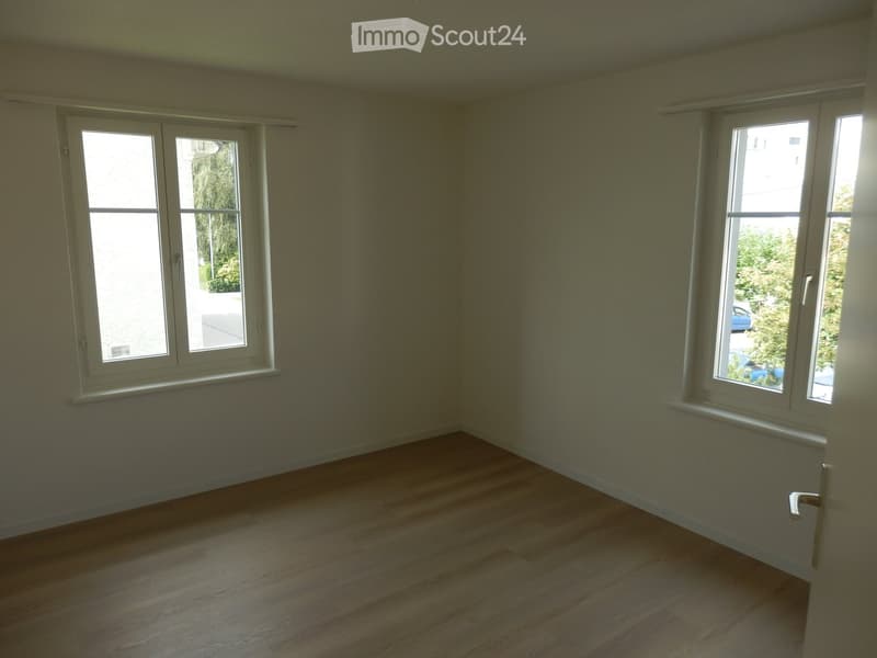 Empty room with wooden flooring and large windows, no furniture or equipment present.
