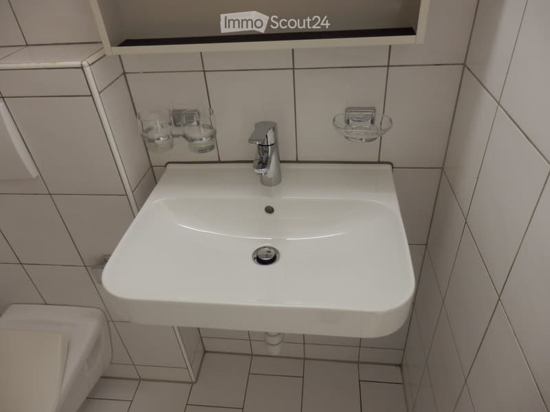A white sink with a modern chrome faucet, mounted on tiled walls with two small glass cups on either side.