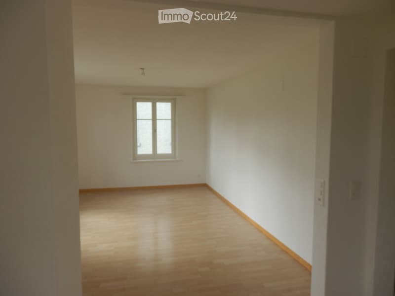 Empty room with wooden flooring, white walls, and a single window allowing natural light.