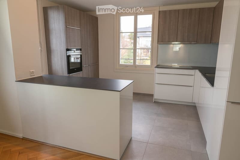 Modern kitchen with white cabinets, a black countertop island, and a built-in oven. The space features a mix of wooden and tiled flooring.