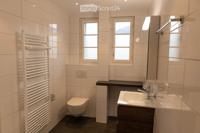 Modern bathroom with white tiles, a toilet, a double sink, a large mirror, and a towel rack.
