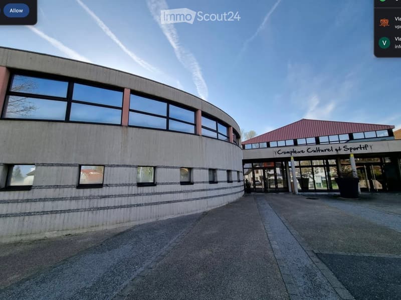 Modern building with a curved facade and large windows, connected to a smaller structure with a red roof and signage reading "Complexe Culturel et Sportif".