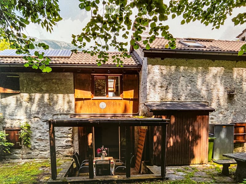 A rustic stone house with wooden accents, featuring a covered wooden deck and outdoor seating area.