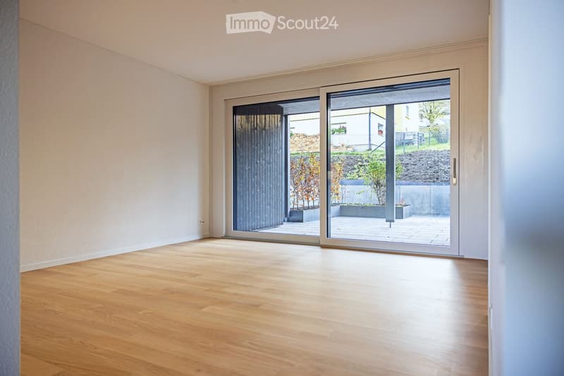 Empty room with white walls, wooden floor, and sliding glass doors leading to a patio.
