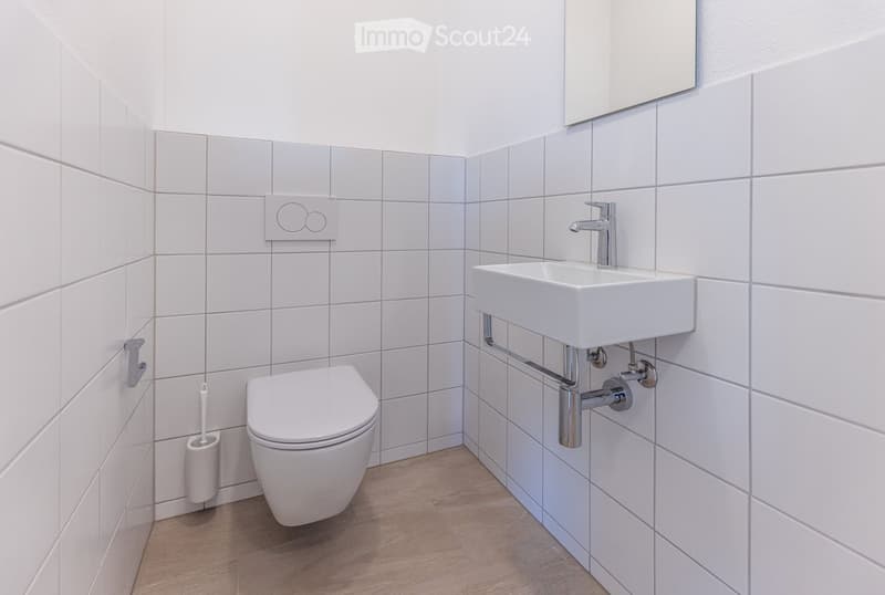 Modern bathroom with white tiles, white toilet, sink, and mirror.