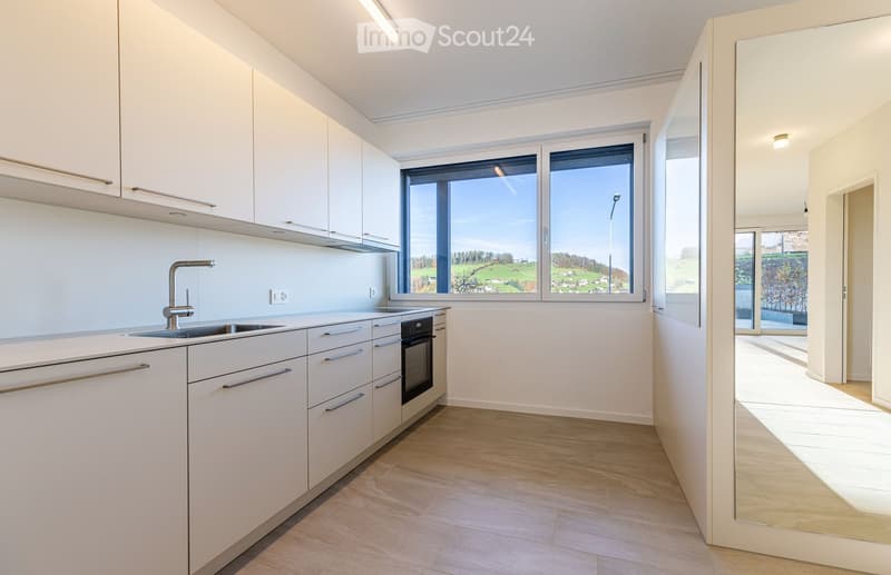 Modern kitchen with white cabinets, a sink, faucet, oven, and large windows.