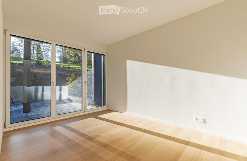 Empty room with white walls, wooden floor, and large sliding glass doors leading to a balcony.