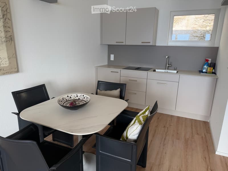 Modern kitchen with white cabinets, a sink, and a dining area featuring a round table and chairs.