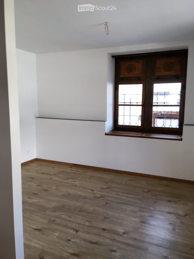 Empty room with wooden flooring and white walls, featuring a large window with decorative glass panels and a small wooden sill.