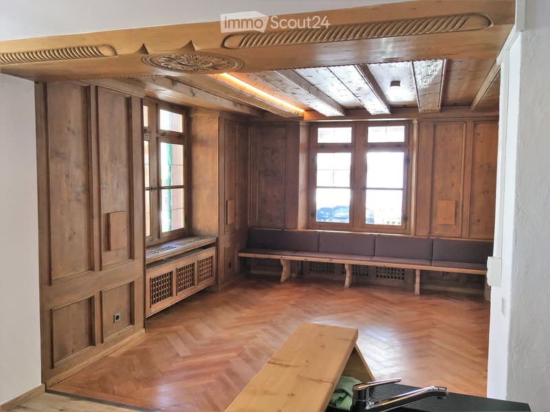 Wooden-paneled room with a long bench, wooden floor, and a sink with a faucet in the foreground.