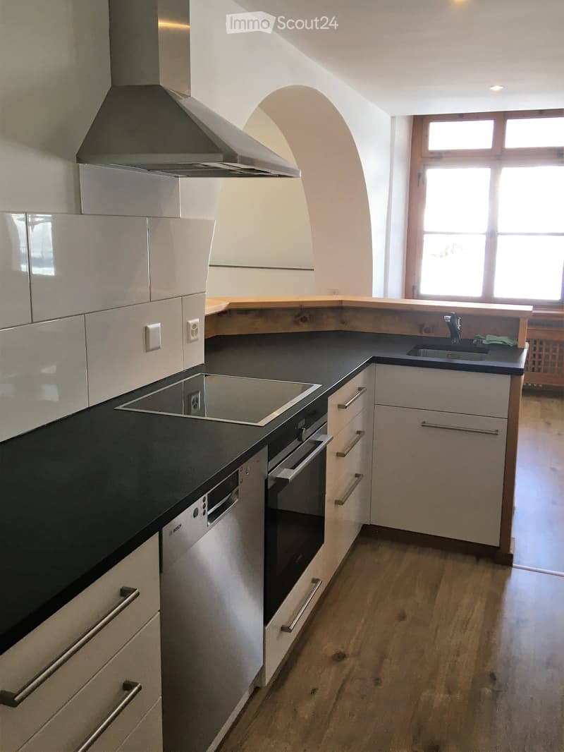 Modern kitchen with white cabinets, black countertops, stainless steel appliances, and wooden flooring.