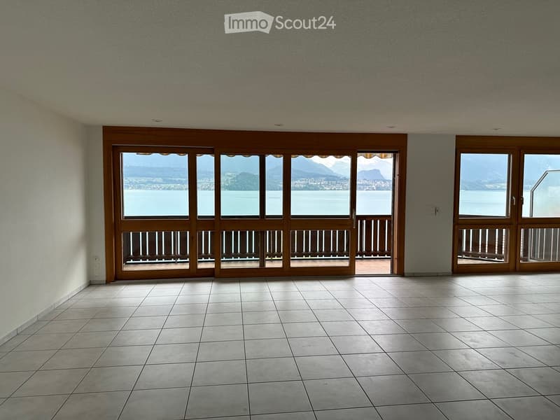 Empty room with tiled floor, large sliding glass doors leading to a balcony with a scenic lake and mountain view.