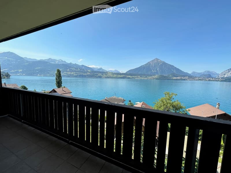 Balcony with wooden railing overlooking a scenic lake and mountain landscape.