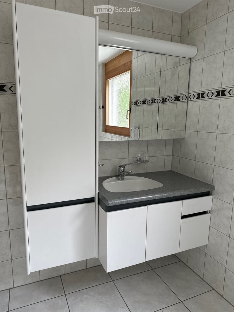 Modern bathroom with a white sink, chrome faucet, white cabinets, and a large mirror above the sink. The walls are tiled with a decorative border near the top.