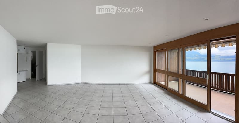 Empty room with tiled floor, white walls, large sliding glass doors leading to a balcony with a scenic lake view.