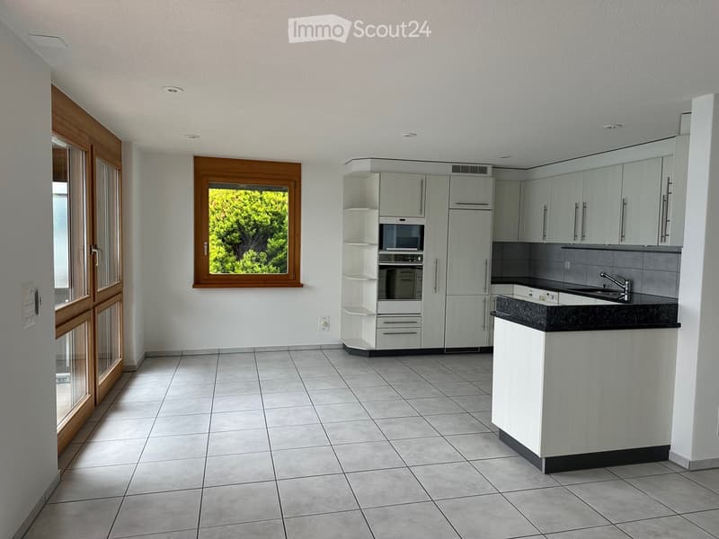 Modern kitchen with white cabinets, stainless steel appliances, and a black countertop. Features a window with wooden frame and a door leading outside.
