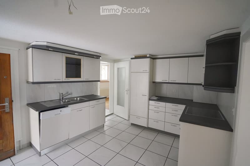 Modern kitchen with white cabinets, black countertops, a sink, a dishwasher, and a refrigerator. The space features tiled flooring and built-in storage.
